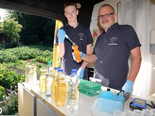 Milan Toups und Harald Gülzow entnehmen einer Wasserflasche eine Probe