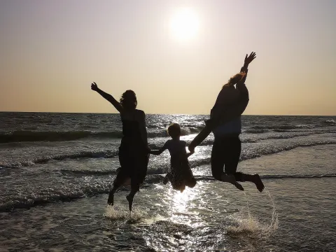 das Bild zeigt zwei erwachsene Personen und ein Kind am Strand
