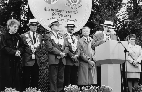 Weezer Kirmes 1996: Unter dem Motto 'Die heutigen Freunde bleiben auch zukünftig Freunde' trug Group Captain Malcolm White die Festkette Mehrere Personen stehen mit Festketten hinter einem Mann am Rednerpult